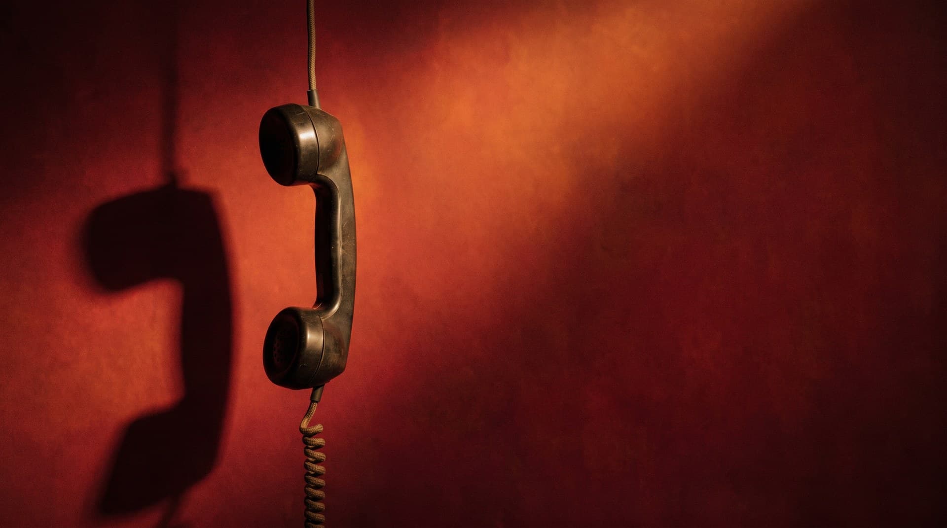 AI voice agent calls flagged as Spam Likely — how to fix caller reputation A telephone handset hanging off the hook against a deep red background, representing outbound calls nobody answers