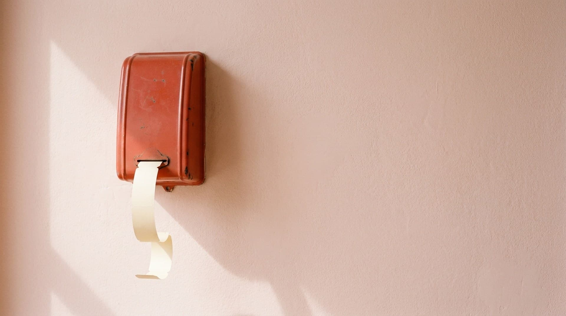 Take a number: pacing n8n requests so the API never says 429 A worn red take-a-number ticket dispenser on a blush pink wall with a curl of paper tickets hanging from it, a metaphor for pacing n8n API requests to stay under a rate limit