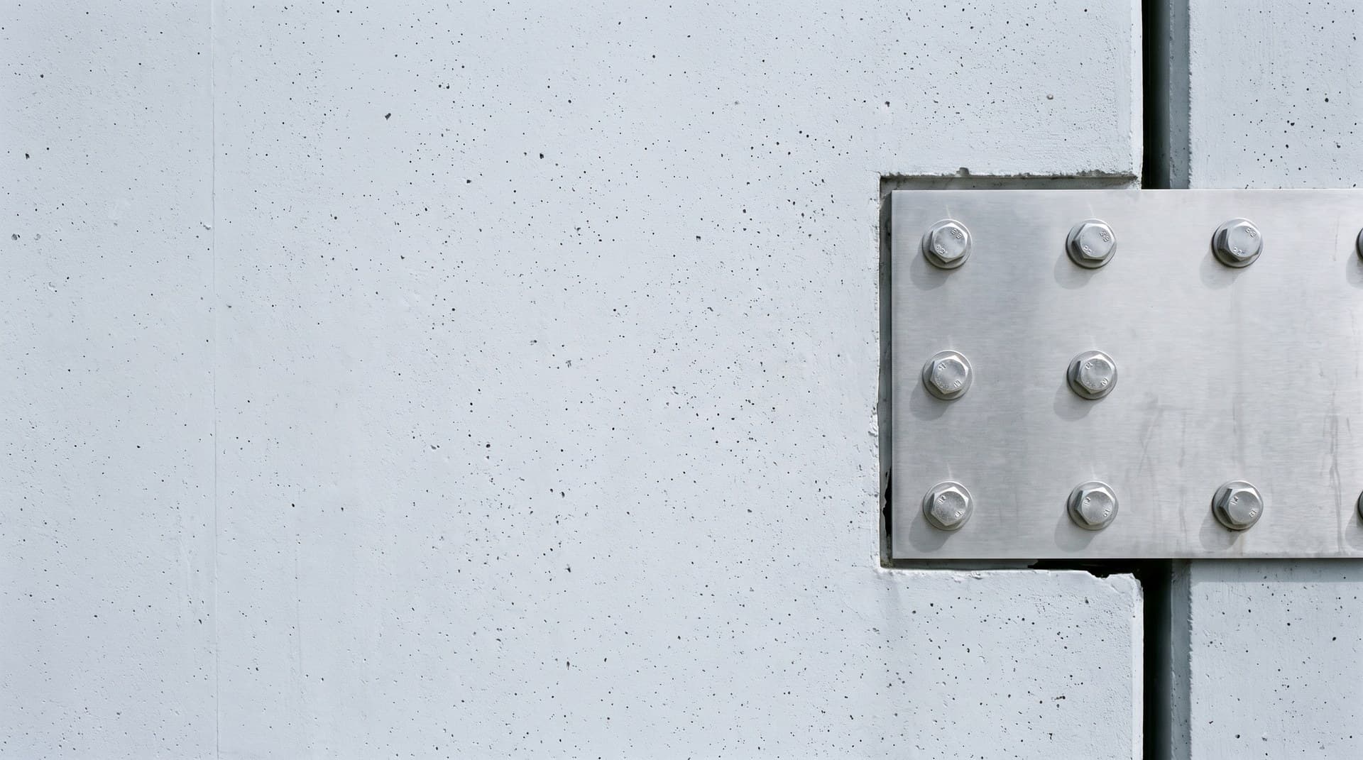Patching a self-hosted n8n instance on n8n's two-week security advisory cadence A freshly bolted stainless steel plate covering a gap in a pale grey concrete wall in flat daylight, representing patching a self-hosted n8n instance